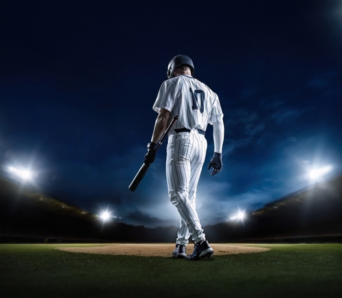 A baseball player standing on the field at night, holding a bat