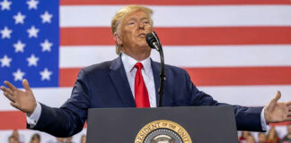 Person speaking at a podium with American flag backdrop.