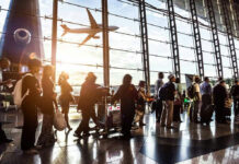 People queuing inside airport terminal with airplane flying outside.