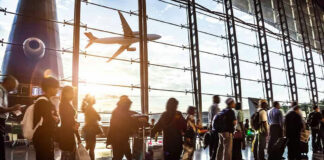 People queuing inside airport terminal with airplane flying outside.