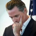 NEWSOM’S Astounding Tax GRAB Targets Trump Supporters… Man in suit thinking with hand on face near a U.S. flag