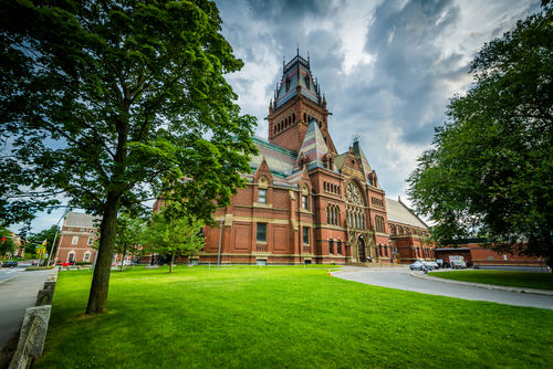 Red-brick Gothic-style building with tall clock tower beside a green lawn