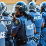 Police officers in riot gear standing in line.