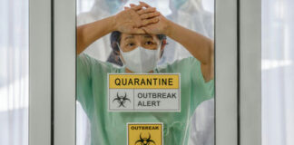 Person wearing mask behind quarantine glass, outbreak alert sign.