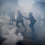 Riot police engaging with protesters amidst clouds of tear gas