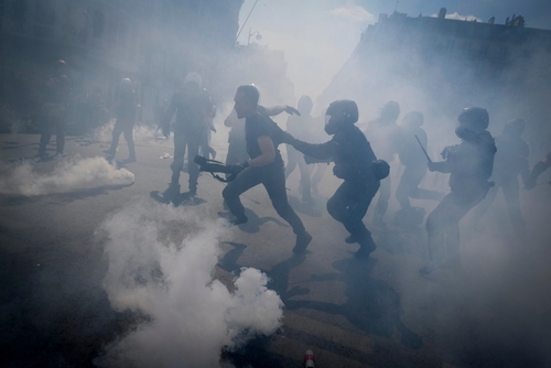 Riot police engaging with protesters amidst clouds of tear gas
