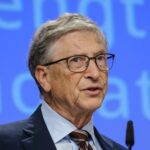 A man in a suit speaking at a conference with a blue background