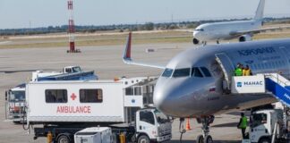 An airplane at an airport with an ambulance and ground crew nearby