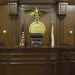 Judges bench in an empty courtroom, scales emblem above.