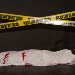 Body under white sheet with police line tape.
