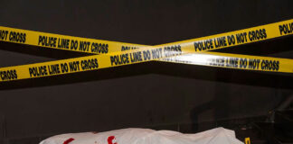 Body under white sheet with police line tape.