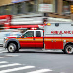 Red ambulance driving quickly through a city street.