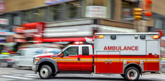 Red ambulance driving quickly through a city street.