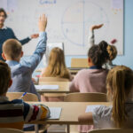 Students raising hands in a classroom as a teacher leads a lesson