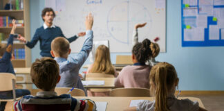 Students raising hands in a classroom as a teacher leads a lesson