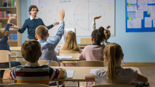 Students raising hands in a classroom as a teacher leads a lesson