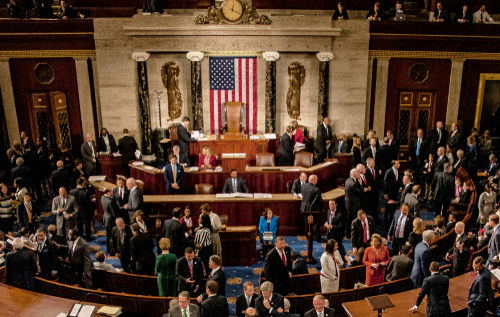 shutterstock_1186368265 Large group in U.S. Congress chamber, American flag displayed.