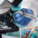 Scientist holding a test tube labeled COVID-19 next to a microscope