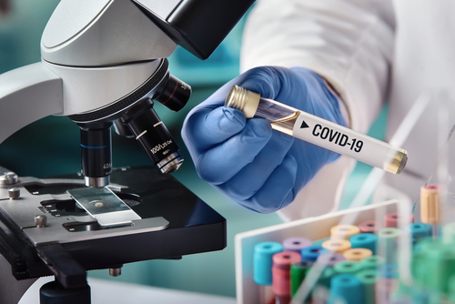 Scientist holding a test tube labeled COVID-19 next to a microscope