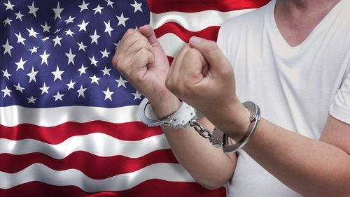 Person in handcuffs raising clenched fists before a United States flag