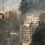 A cityscape showing damaged buildings and thick smoke rising from the ground