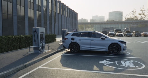 A silver electric vehicle charging at a station in a parking lot