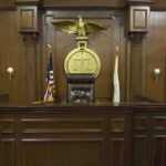 Affairs, Abuse, Escape Plot? Prosecutor Booted Judges bench in an empty courtroom, scales emblem above.