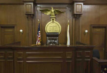Affairs, Abuse, Escape Plot? Prosecutor Booted Judges bench in an empty courtroom, scales emblem above.