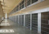 Empty prison cell block with barred doors and walkway.