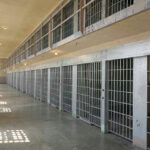 Empty prison cell block with barred doors and walkway.