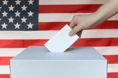 2496142057 Hand casting ballot into box before U.S. flag