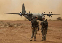War Drums Over Jordan — Real Or Hype? Two soldiers watch a military transport plane on a dusty airstrip