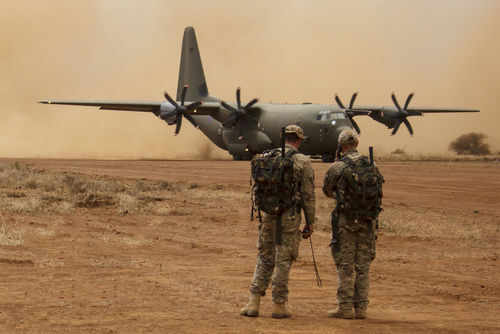 shutterstock350545301jpg Two soldiers watch a military transport plane on a dusty airstrip