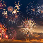 Colorful fireworks display against a darkening evening sky.