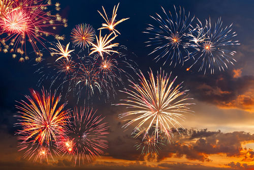 Colorful fireworks display against a darkening evening sky.
