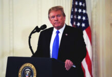A man in a suit standing at a podium with the presidential seal, in front of an American flag