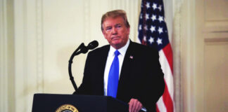 A man in a suit standing at a podium with the presidential seal, in front of an American flag