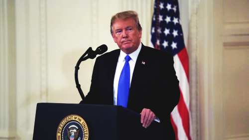A man in a suit standing at a podium with the presidential seal, in front of an American flag