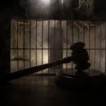 A gavel placed on a wooden surface in front of a barred cage with a smoky background