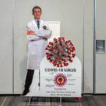 Pulmonary Infarction? Fauci’s Quiet Vaccine Crisis Cardboard cutout of doctor with COVID-19 virus info display