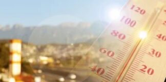 Close-up of a thermometer in hot sun over a blurred road and mountains
