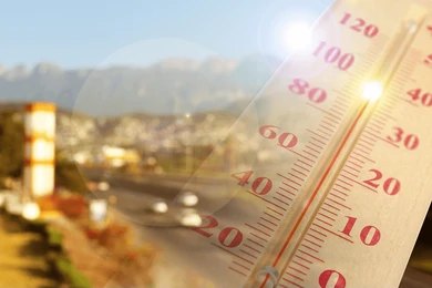 shutterstock_2699035875 Close-up of a thermometer in hot sun over a blurred road and mountains