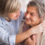 Two older women embracing and smiling on a couch