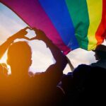 Crowd under a rainbow flag at sunset