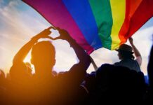 Crowd under a rainbow flag at sunset