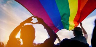 Crowd under a rainbow flag at sunset