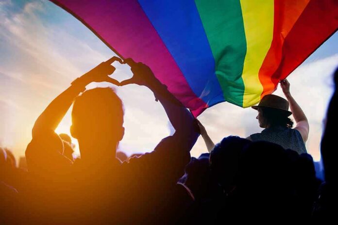 Crowd under a rainbow flag at sunset