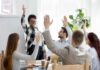 Team in meeting raising hands around a smiling presenter