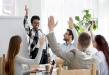 Team in meeting raising hands around a smiling presenter