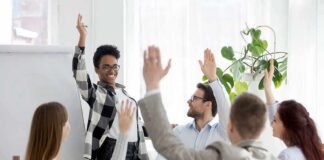 Team in meeting raising hands around a smiling presenter